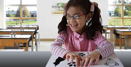 Student exploring tactile reading material at a desk.